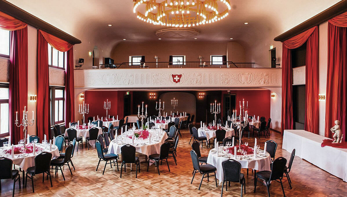 Casinosaal mit gedeckten runden Tischen, roten Vorhängen und einer Empore